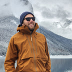Man wearing a brown jacket and sunglasses with a mountainous landscape in the background