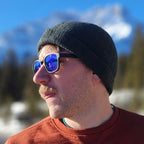 Man wearing a black beanie and blue sunglasses with a mountainous background